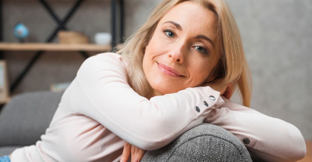 Mulher meia idade sentada no sofá e sorrindo, com clima de paz e segurança. Resveratrol Anti envelhecimento.